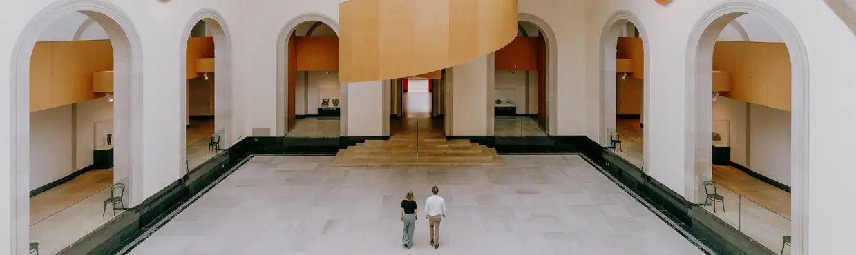 Geräumiger Innenraum der Art Gallery of Ontario mit großen Torbögen, hohen Decken und einer markanten hölzernen Wendeltreppe in der Mitte.