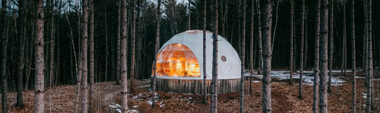 A dome cabin tucked among evergreens at Glen Oro Farm, seen from above on a winding trail with patches of melting snow.