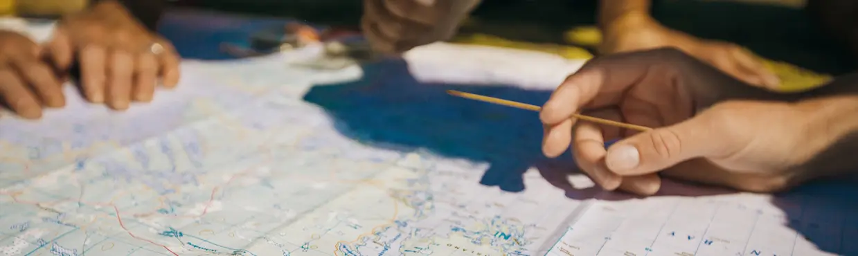 Hands pointing at a detailed map spread out on the ground, mapping out a Georgian Bay kayaking route.