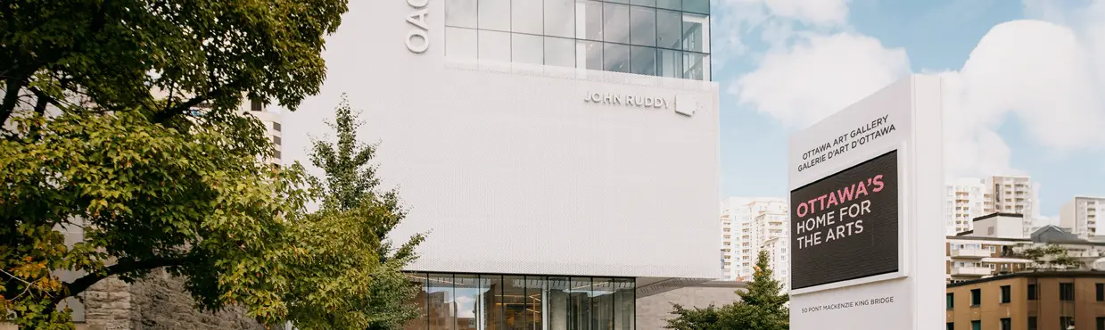 Two people walking toward the modern glass entrance of the Ottawa Art Gallery on a sunny day.