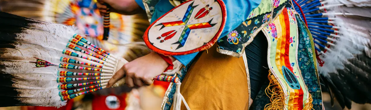 Close-up of a powwow dancer in colourful regalia holding a feather fan during a cultural performance at the Canadian Museum of History.