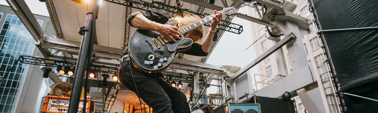 Groupe de rock sur la place Yonge-Dundas, à Toronto, avec un guitariste en plein saut près de ses camarades et d'immeubles en arrière-plan.