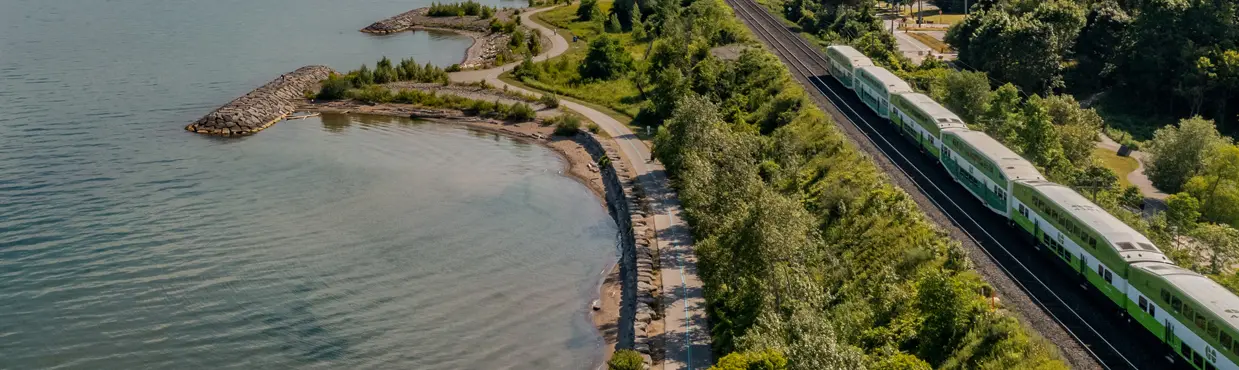 토론토 광역권의 무성한 녹지 사이로 온타리오 호수 해안선을 따라 달리는 GO 열차와 루즈 비치와 루즈 강 공원의 공중 사진입니다.