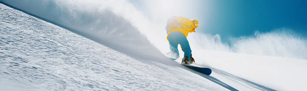 맑은 푸른 하늘을 배경으로 햇살이 잘 드는 경사면에서 신선한 눈가루를 헤치며 밝은 장비를 착용한 스노보더.