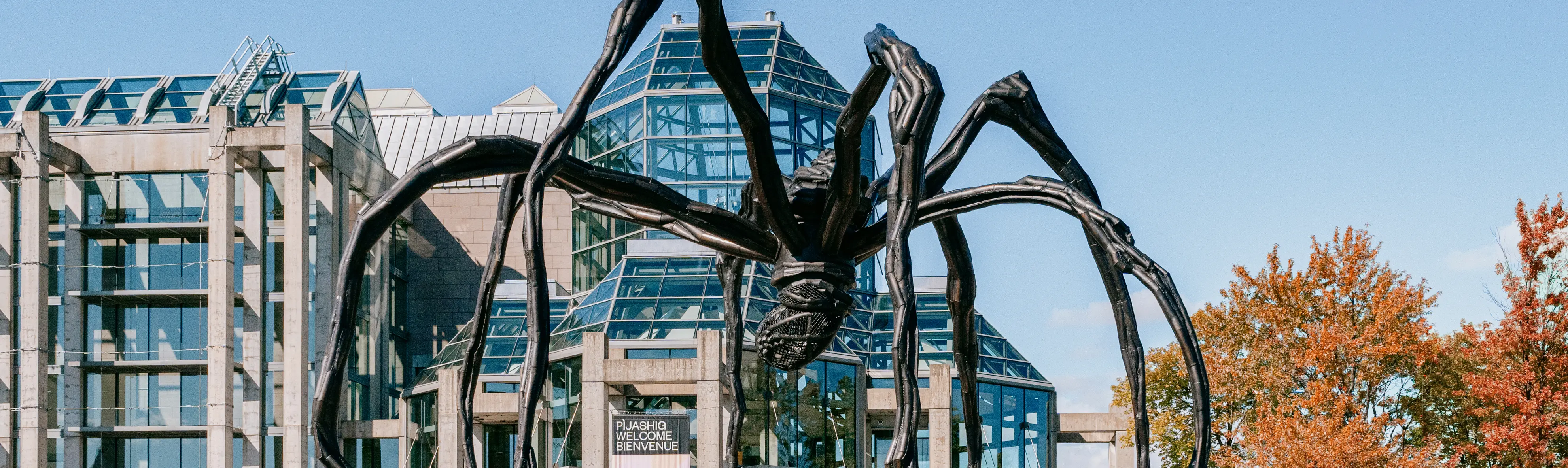 Grande sculpture d’araignée en bronze aux côtés d’un bâtiment contemporain avec des pyramides en verre.