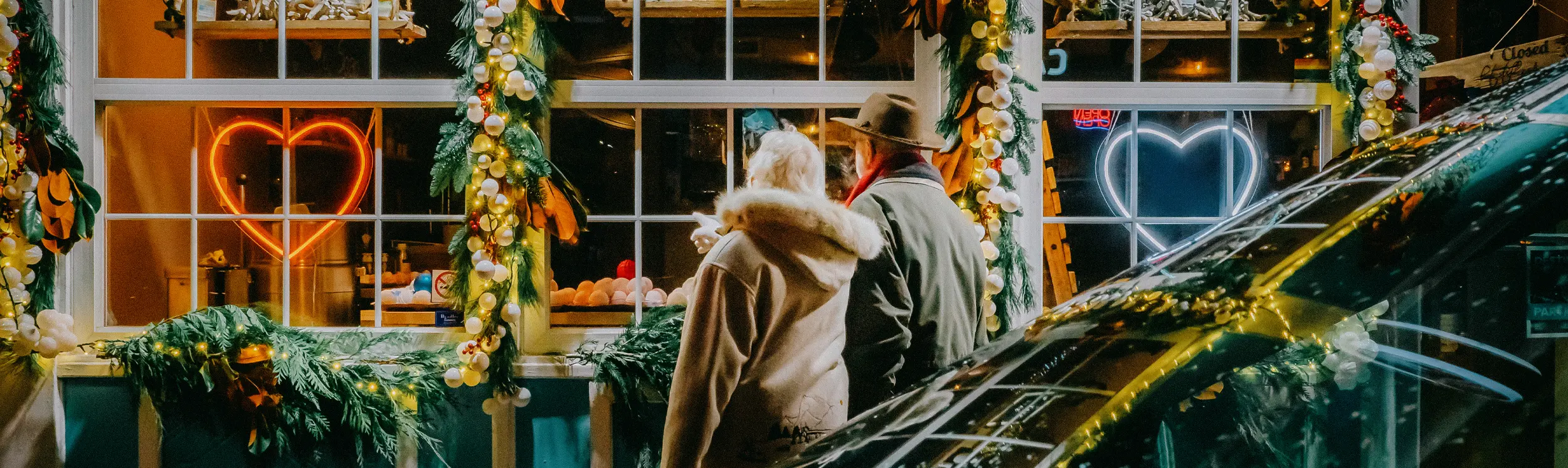 A couple walks past the windows of a store lit up and decorated for the holidays.