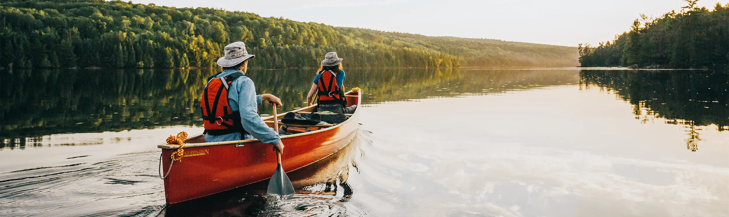 Zwei Personen paddeln in einem roten Kanu über einen ruhigen, von Wald umgebenen See.