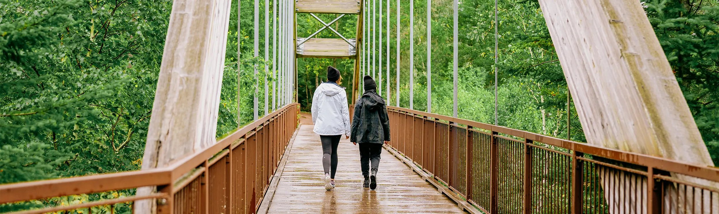 森に囲まれた木製の吊り橋を二人が歩いている。