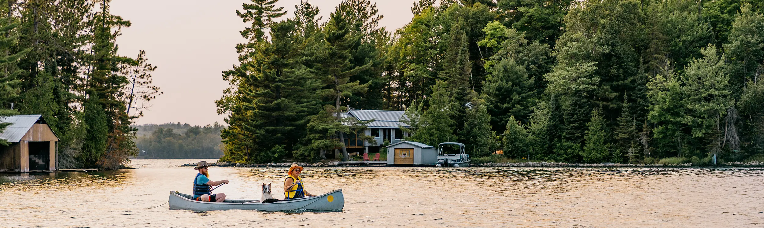 Deux personnes en canot sur un lac paisible entouré d’une dense forêt du Nord et de petits chalets.