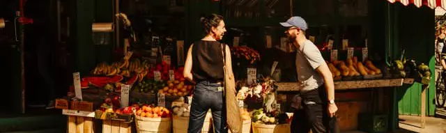 Dos personas conversando frente a un puesto de productos agrícolas.
