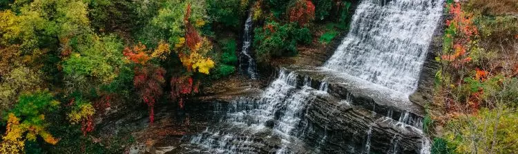 Luftaufnahme eines Wasserfalls, umgeben von herbstlichen Farben. 