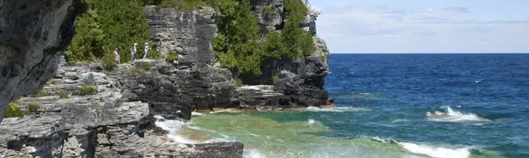 Tres personas caminan a lo largo de una costa rocosa con vistas al agua azul de la Bahía Georgian.