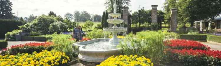 A couple walk past an ornate fountain surrounded by flower beds at Royal Botanical Gardens.