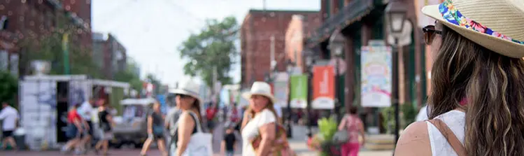 Der Hinterkopf einer Frau, die auf eine Kopfsteinpflasterstraße blickt, die zwei andere Frauen überqueren.