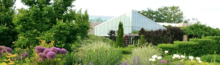 Üppige Büsche, Sträucher, Blumen und Bäume umgeben ein Glasgebäude im Toronto Botanical Garden.