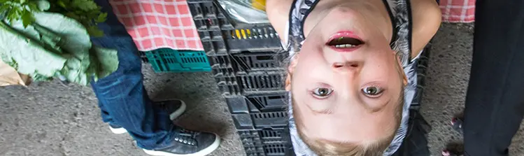 A young girl looks up from a vendors table at a farmers’ market.