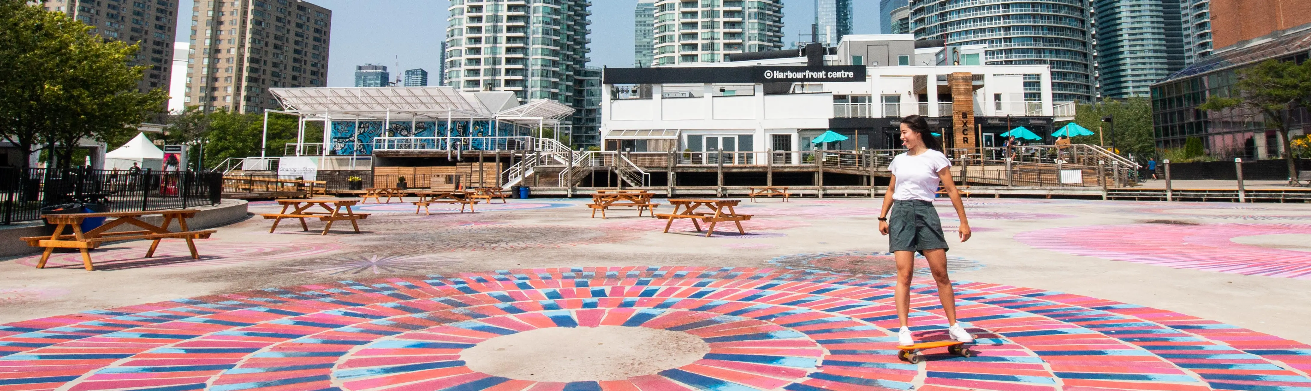 Eine Person fährt auf dem bunten Bürgersteig vor dem Harbourfront Centre Skateboard. 