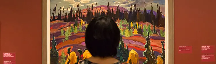 A woman stands in front of a Group of Seven painting. 