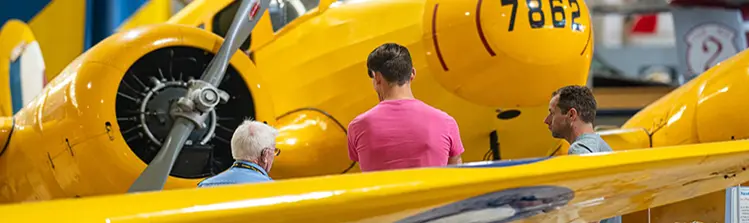 Three people view a vintage aircraft at an aviation museum.