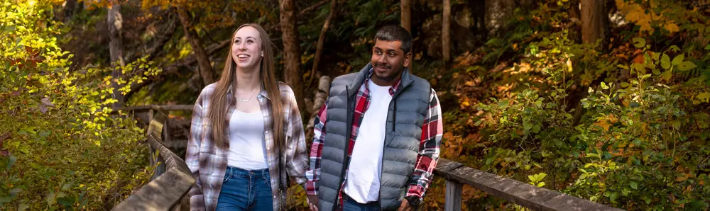 가을에 한 커플이 숲 속 나무 판자길을 걷고 있다.