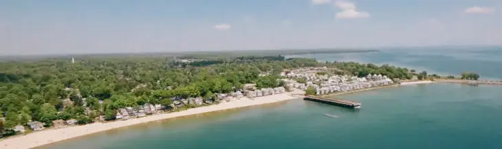 Vue aérienne de la plage Crystal avec ses eaux bleues, sa rive de sable et ses rangées de charmantes maisons au bord de l’eau, sous un ciel radieux.