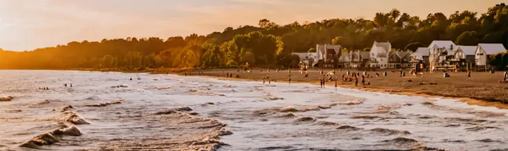 Olas rodando hacia la playa de Port Stanley, donde bañistas y amantes del sol disfrutan del atardecer, con encantadoras cabañas y un entorno arbolado.