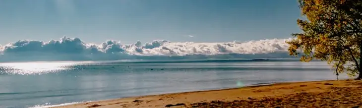 ターキー ポイント ビーチの晴れた朝。前景には金色の砂浜が広がり、穏やかな海には青い空と雲が映っています。