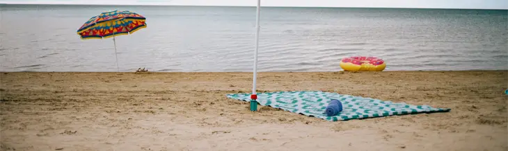 Sombrillas de rayas y una manta estampada colocadas en la orilla arenosa de la playa de Wasaga, con aguas tranquilas y un cielo nocturno melancólico.