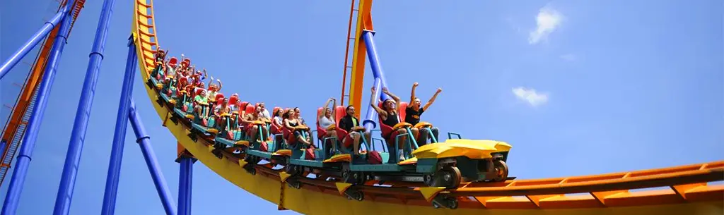 Groupe de personnes, les mains en l’air, à bord d’une montagne russe jaune, orange et bleu à Canada’s Wonderland.