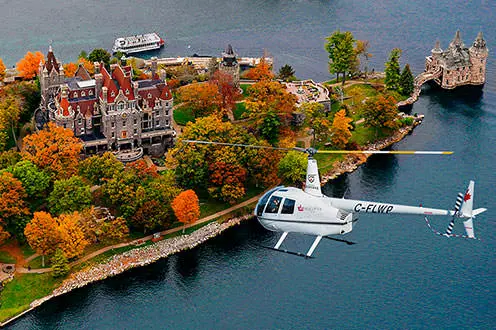 Una vista de pájaro de un helicóptero que sobrevuela el castillo de Boldt en las 1000 islas. El castillo está rodeado de árboles de color naranja, rojo y verde brillante y se encuentra a orillas del lago.