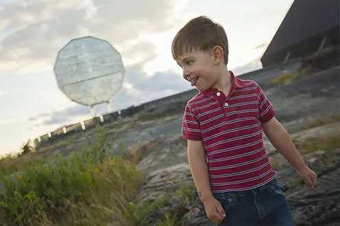 Un niño sonríe en primer plano del Big Nickel que domina el cielo detrás de él.