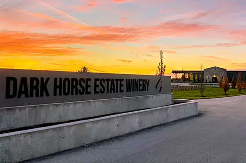 Cartel de Dark Horse Estate Winery con el edificio de la bodega en la distancia durante una puesta de sol.