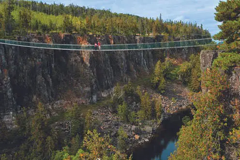 A couple stands in the middle of a suspension bridge across a wide canyon