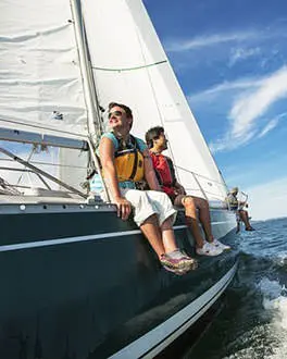Sailors sit on the side of a sailboat as they enjoy a sunny day