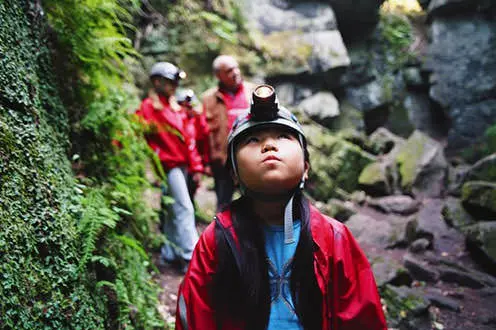 Child with hard hat and head lamp looking up in cave