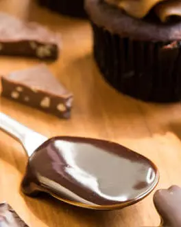 A close up of metal spoon covered in chocolate, surrounded by a chocolate cupcake and chocolate bark.
