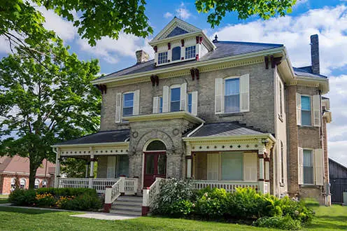 A large victorian buff brick house surrounded by trees and  manicured grounds. 