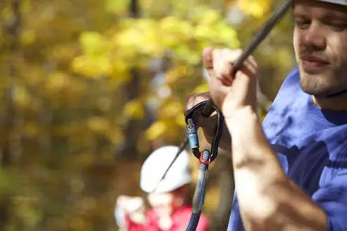 An adventurer clasps in a safety hook while ziplining through a forest
