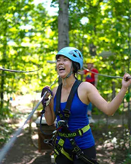 Una mujer que lleva un arnés se ríe mientras está atada a tirolinas en un bosque.