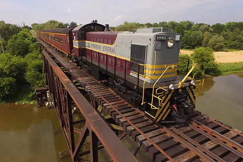 A large heritage train crosses a train bridge over a wide river. 