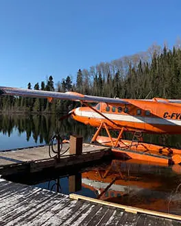 Ein orangefarbenes Wasserflugzeug, das an das Dock am Ufer eines Sees gebunden ist.