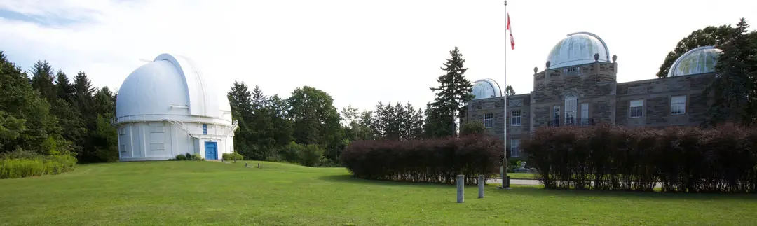 Zwei Gebäude und ein Fahnenmast, die zum David-Dunlap-Observatorium gehören, sind von einem gepflegten Rasen und Garten umgeben.