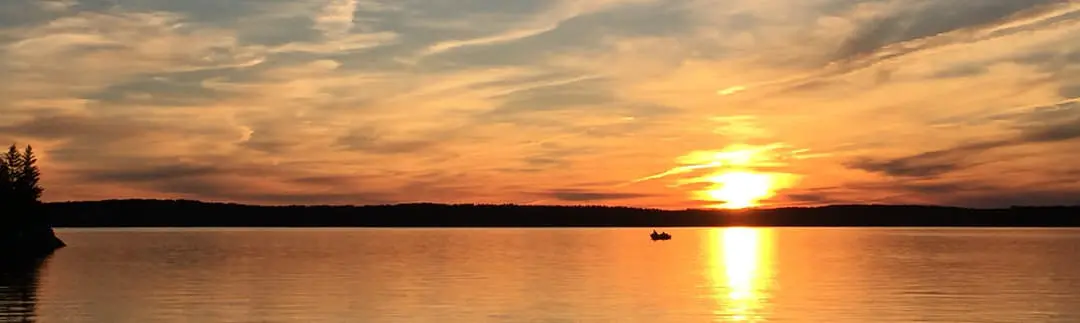Dos pescadores en un barco en un gran lago bajo un cielo espectacular al atardecer