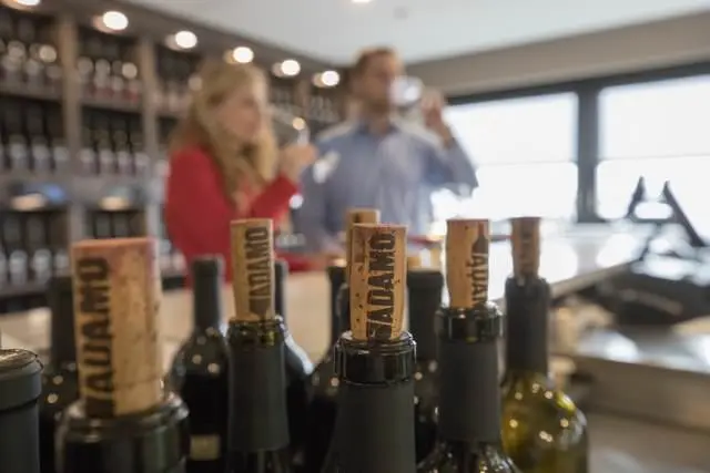 Corchos en botellas de vino, mientras un hombre y una mujer disfrutan del vino en el fondo