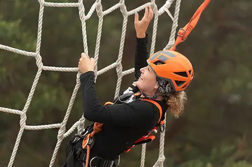 A close up of a woman wearing a helmet and a harness while grabbing onto a large net made from rope.