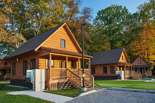 Rangée de chalets abordables entourées d'herbe et d'arbres, de construction récente, chacun possédant sa propre place de stationnement en gravier.