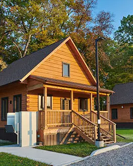 A row of newly built accessible cabins each with their own gravel parking spots and surrounded by grass and trees. 