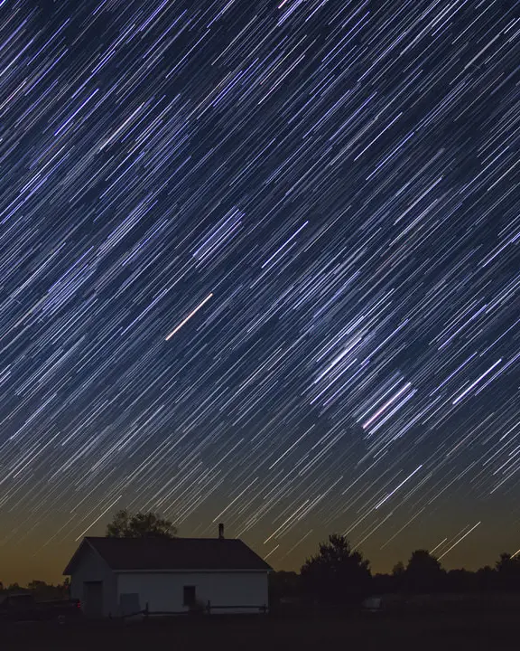 A dramatic show of stars illuminates the dark sky over a rural farm scene