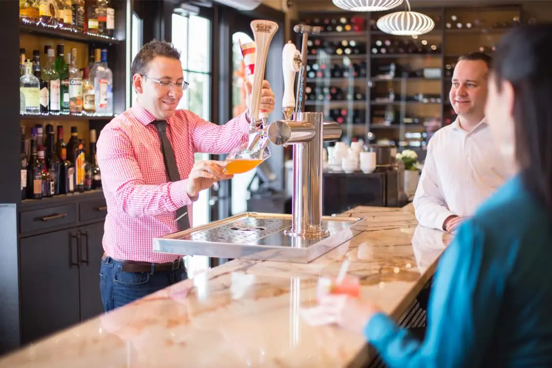 Barman dans un bar moderne qui sert une consommation à des clients souriants.