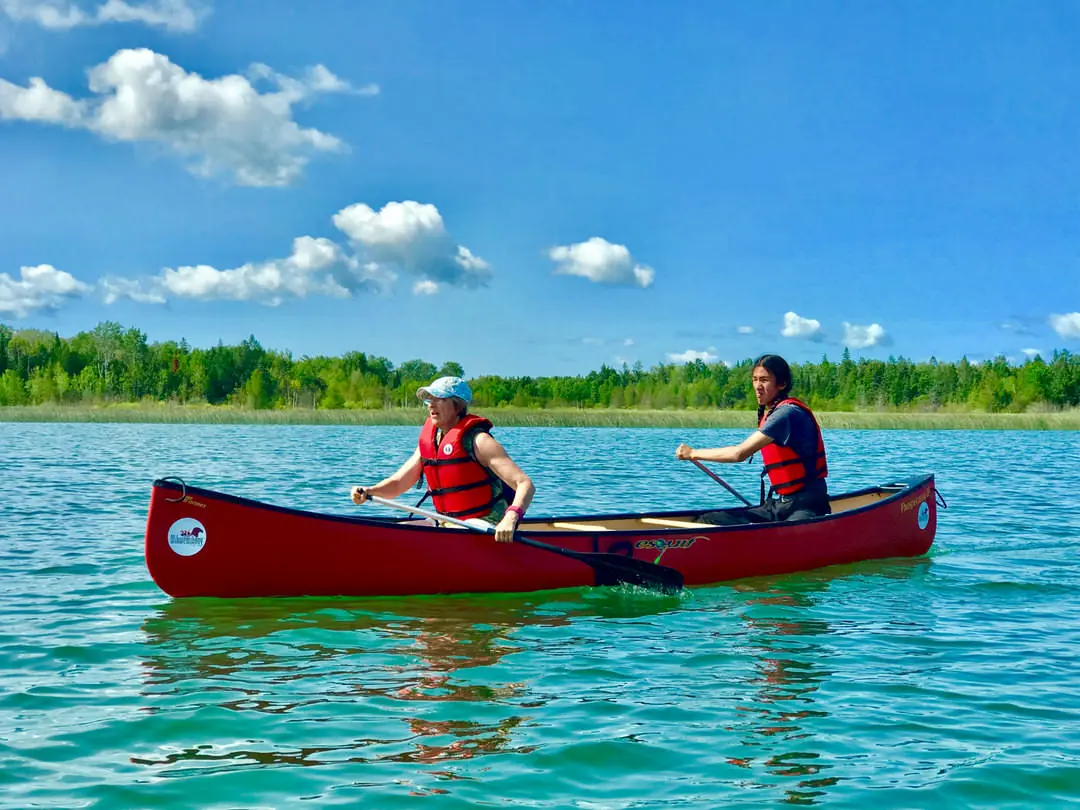 Deux canoéistes qui pagaient sur une étendue d'eau le long d'une rive boisée.
